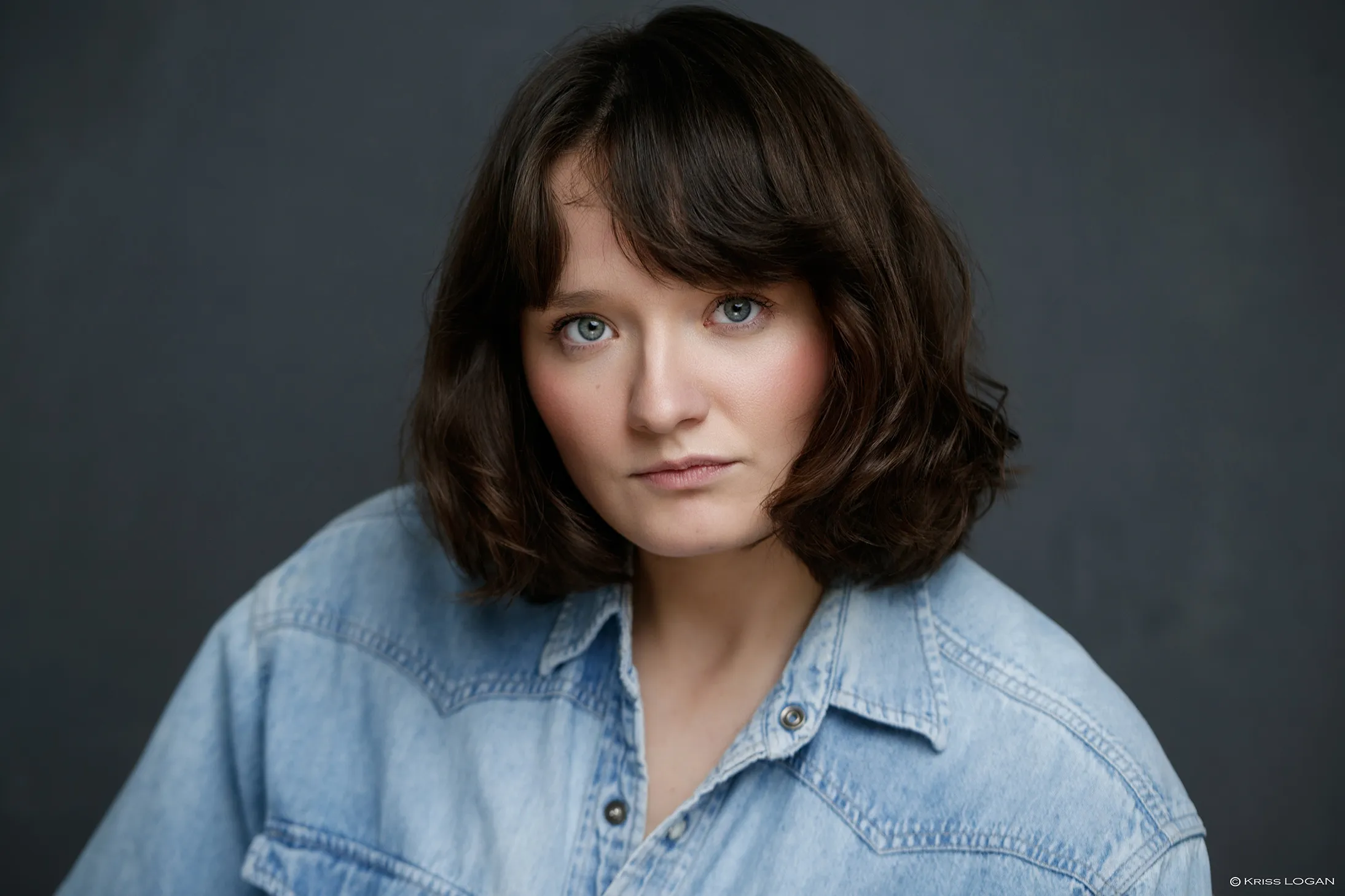 Portrait au regard intense, chemise en denim clair, fond gris bleuté.