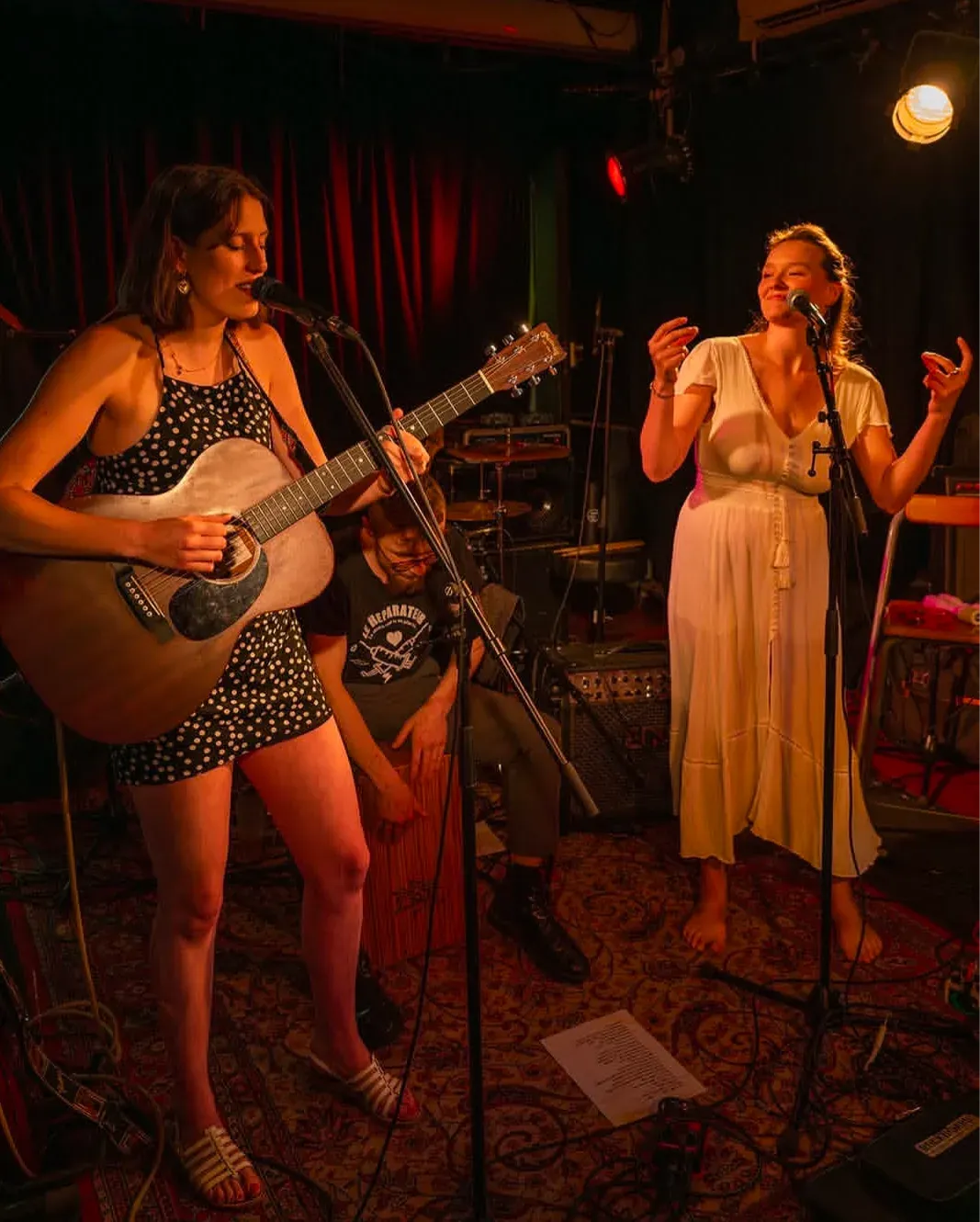 Duo on stage, a guitarist and a singer in a white dress, a percussionist on cajón.